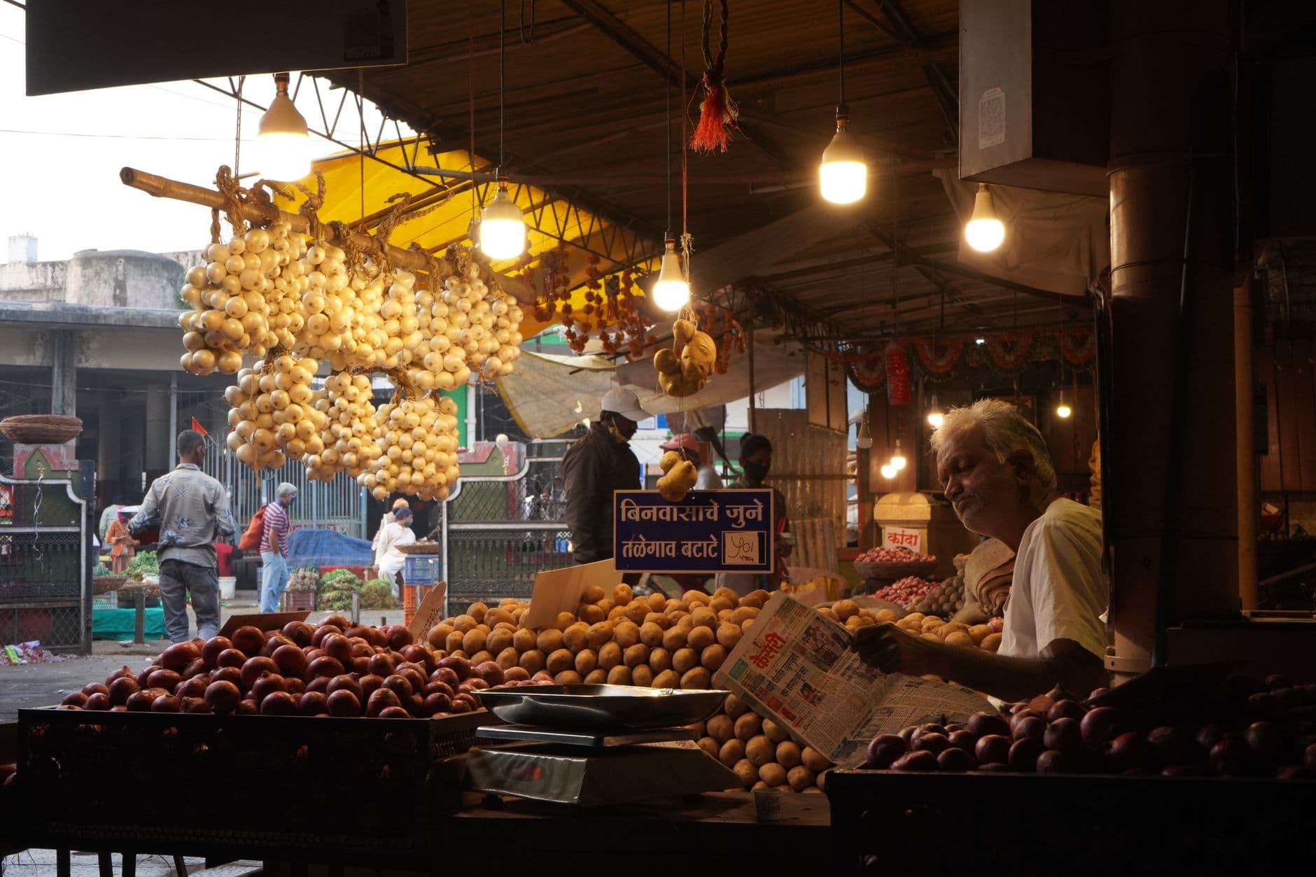 Grocery & Quick Commerce Websites — A vendor reads a newspaper in a bustling Indian market filled with fresh produce and vibrant ambiance.