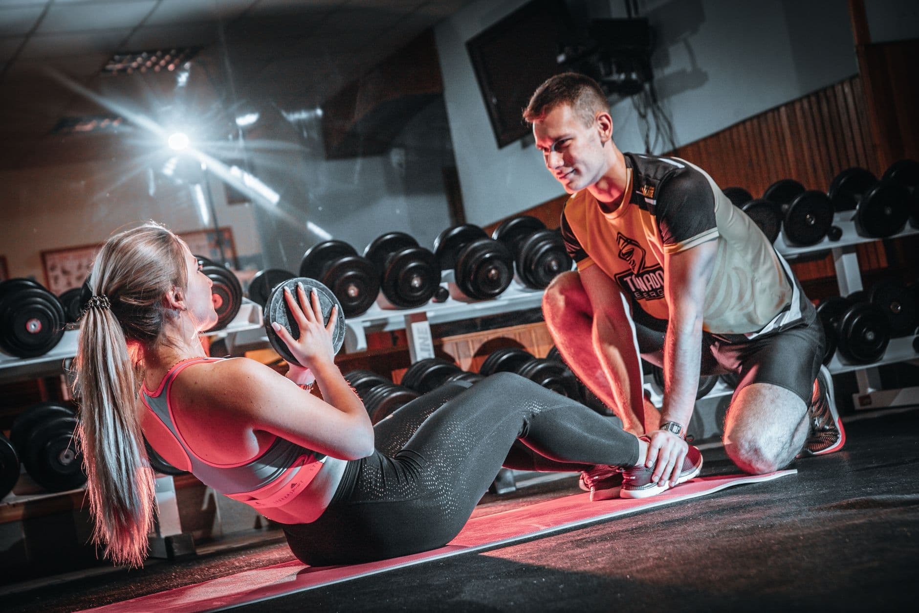 Gym & Fitness Websites — A personal trainer assists a woman doing sit-ups with a medicine ball in a gym setting.