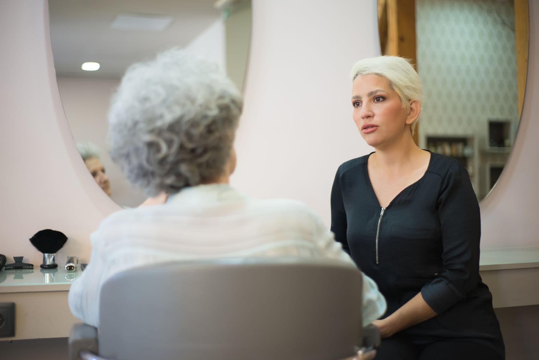 Salon Appointment Websites — Two women having a conversation in a salon setting with a mirror reflecting their interaction.