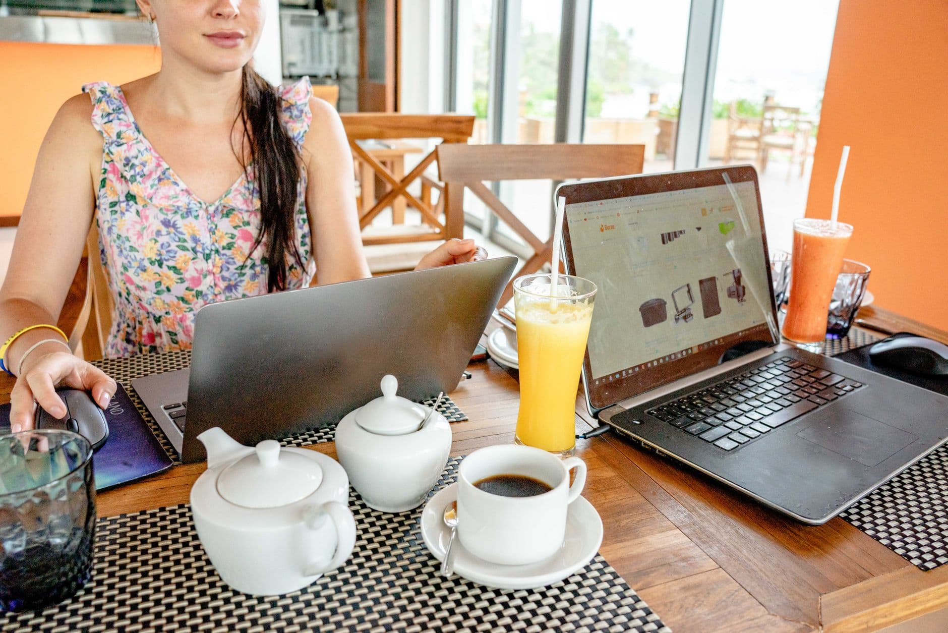 VPS Hosting for Freelancers — A woman working on laptops at a cafe with drinks and teapots, showcasing a remote work lifestyle.