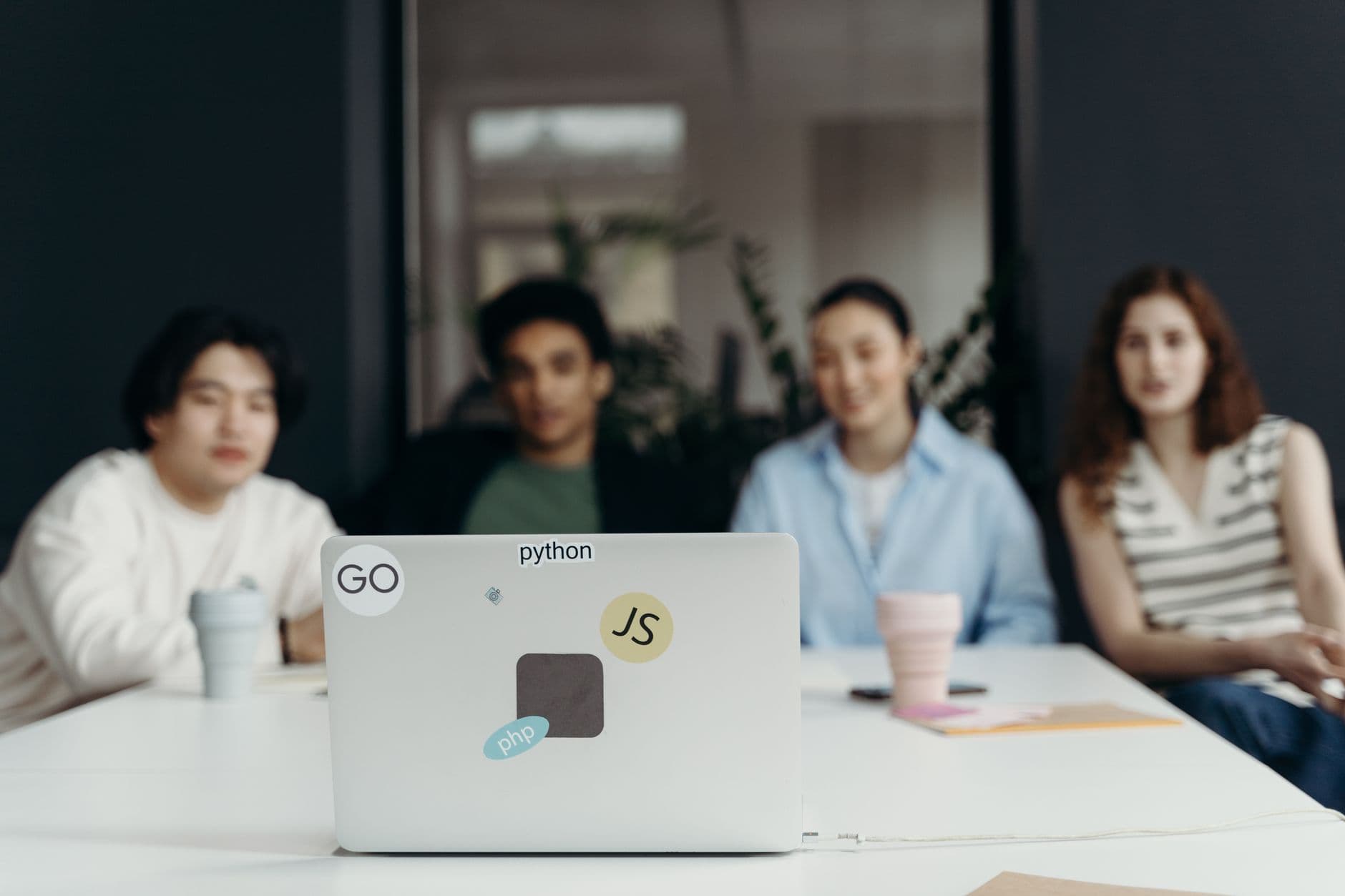 VPS Hosting for Software Companies — A focused group meeting in an office setting with diverse team members and a laptop featuring tech stickers.