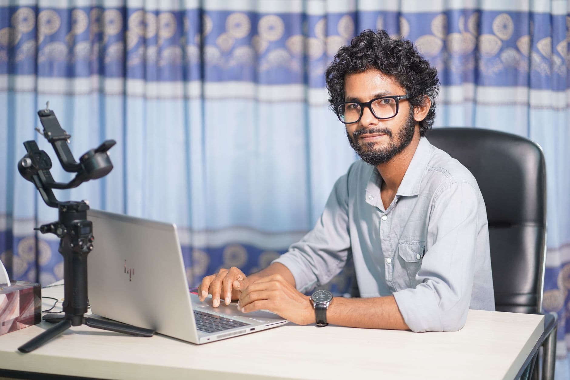 VPS Hosting for Web Designers — Portrait of a web developer with a laptop and camera, working at his office desk in a modern setup.