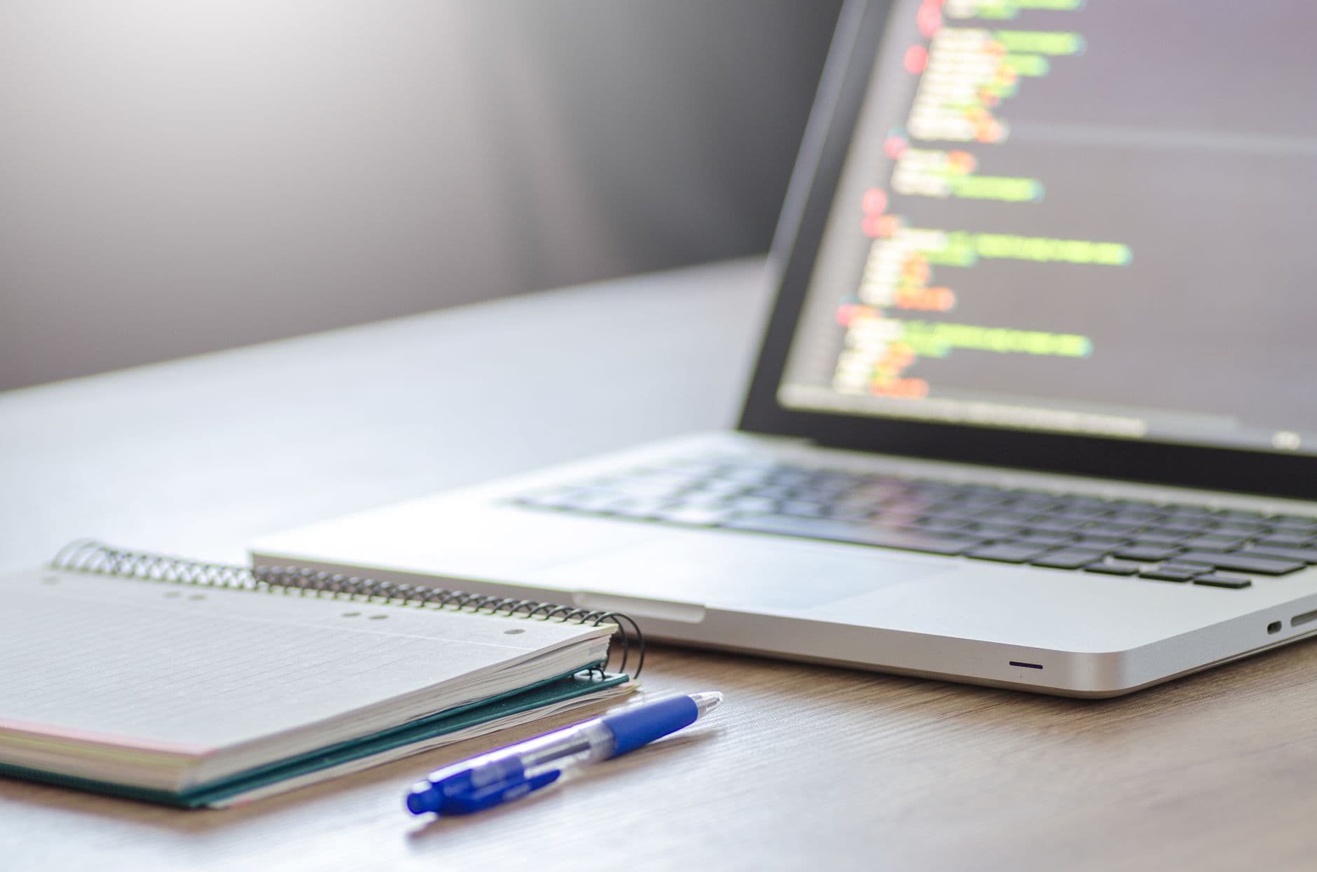 VPS Hosting for Web Designers — Open laptop with programming code on screen next to a notebook and pen on a desk.