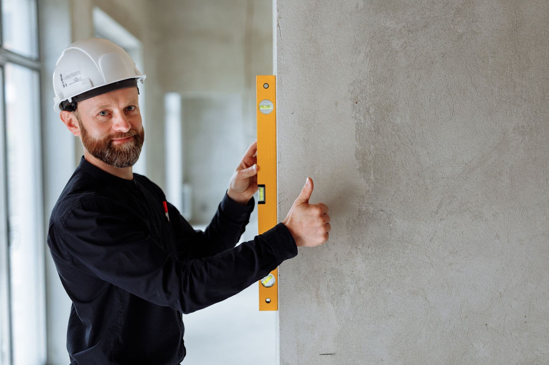 Website & Hosting for Contractors — Confident male construction worker using a spirit level on a concrete wall for precise alignment indoors.