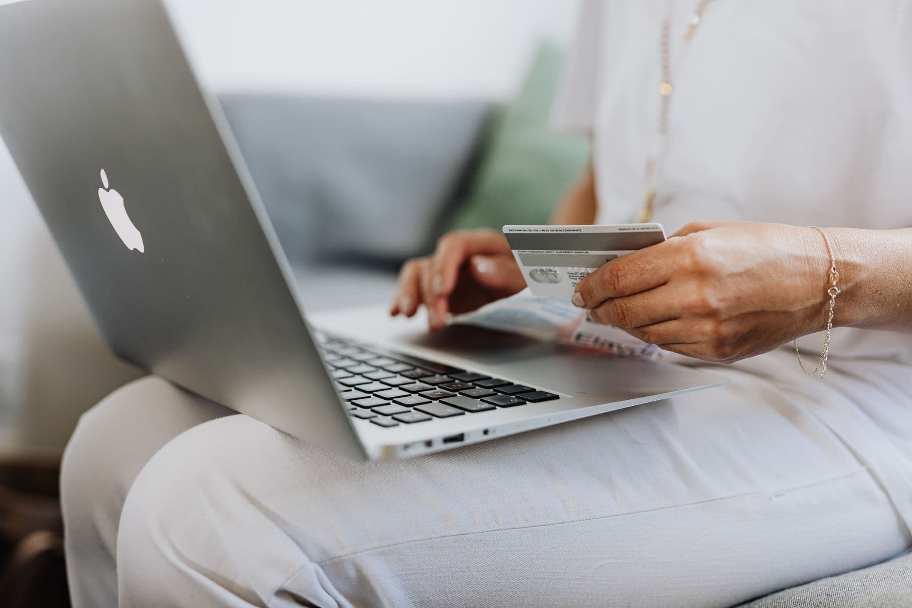 E-commerce Development — Close-up of a person holding a credit card while shopping online using a laptop at home.
