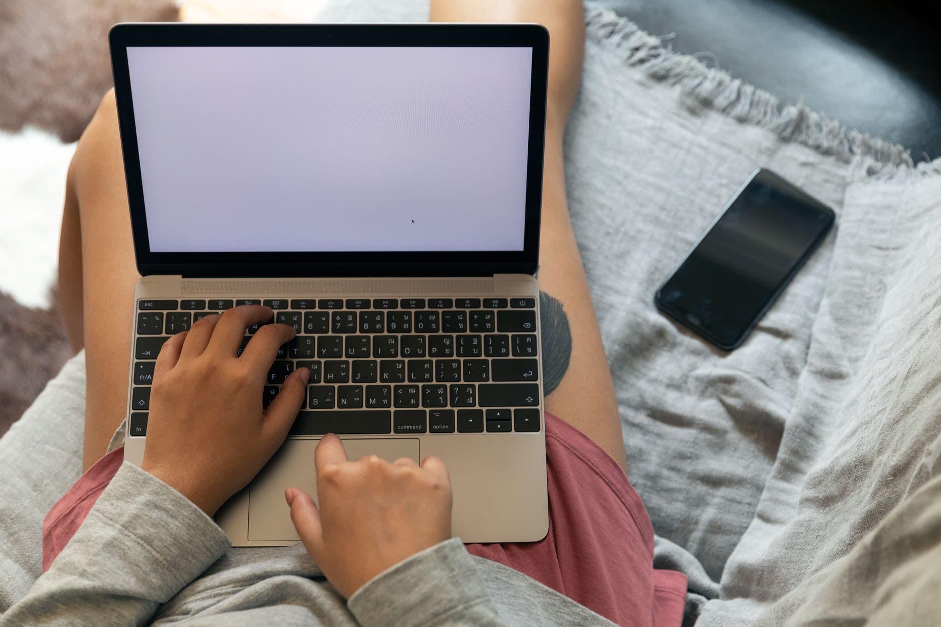 Email Marketing — From above of crop faceless female remote employee typing on netbook with empty screen while sitting near smartphone in apartment