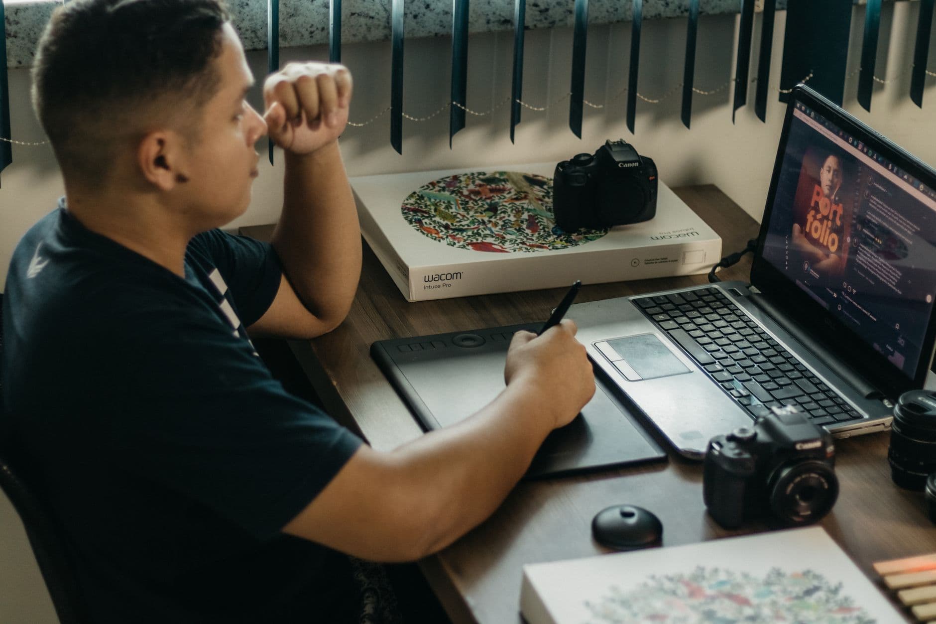 Graphic Design — A photographer working at a creative setup with a laptop and Wacom tablet, focused on editing photos indoors.