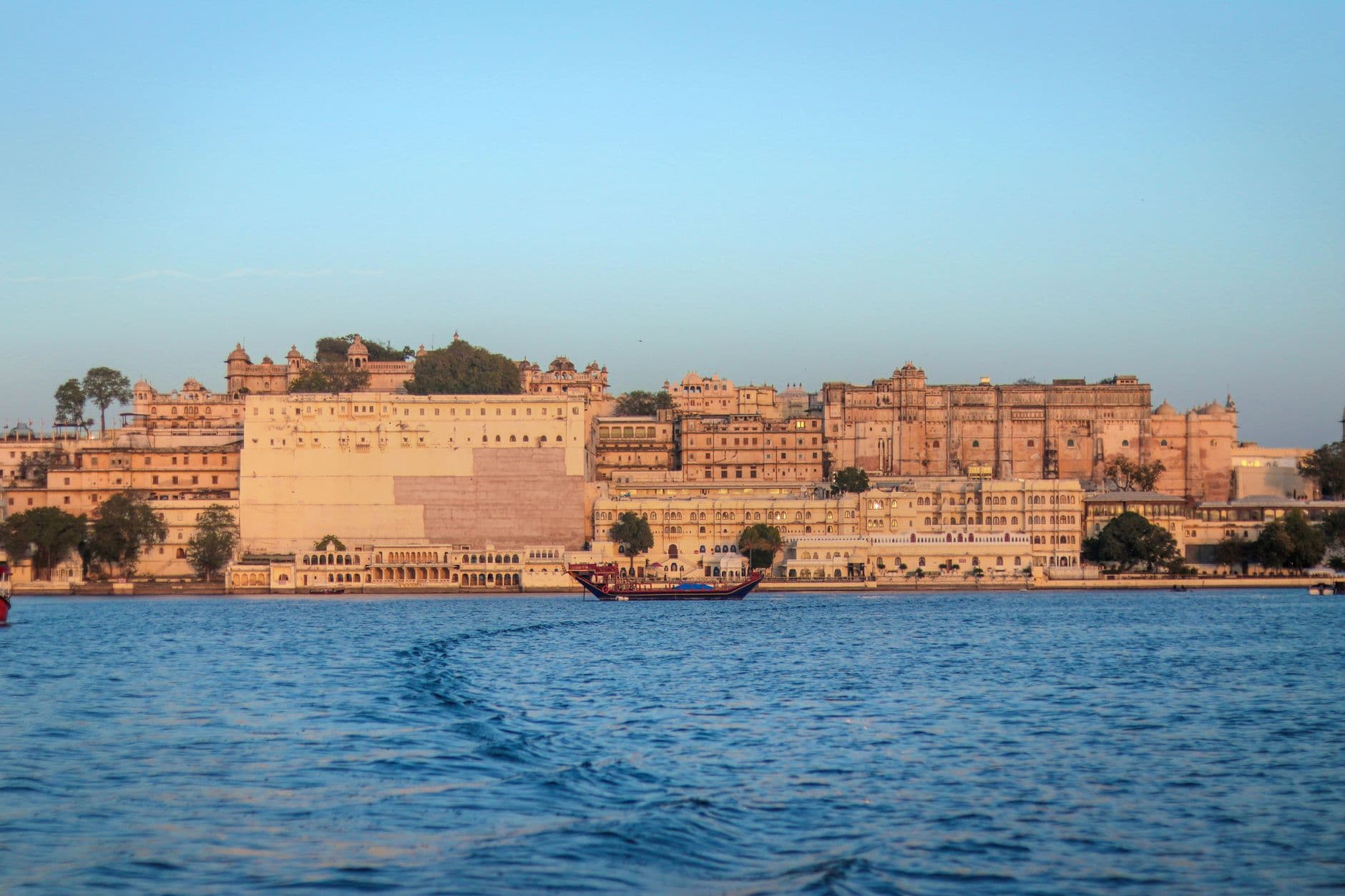 Travel Agency Websites — View of the historic Udaipur City Palace in Rajasthan, India, across Lake Pichola during sunset.