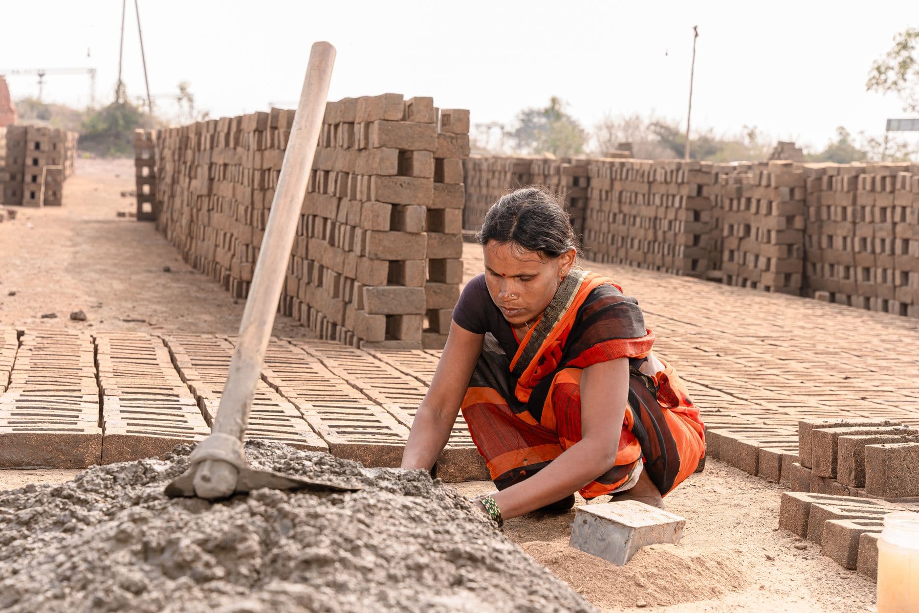 Website & Hosting for Builders — A woman manually shaping bricks in an outdoor Indian factory setting.
