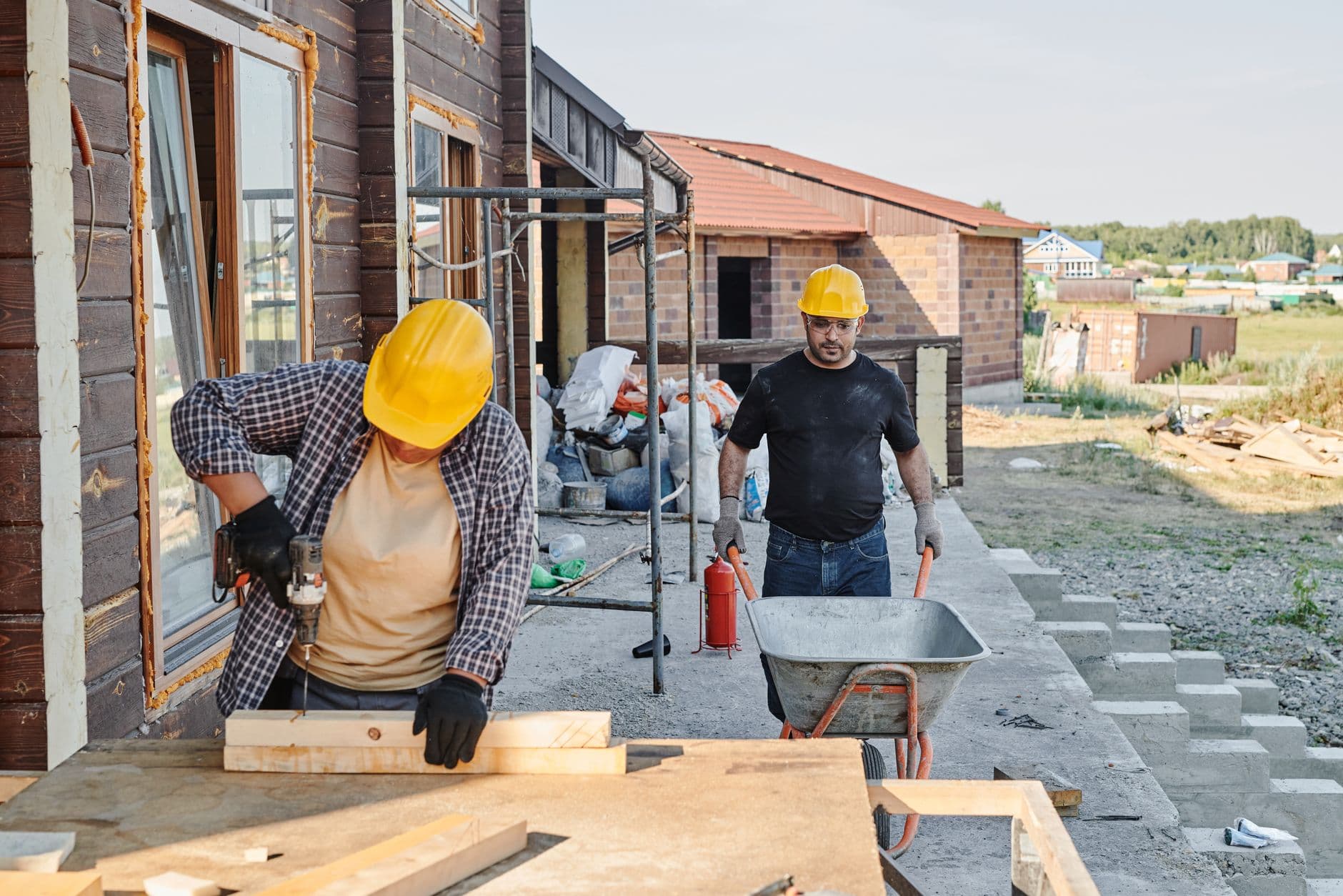 Website & Hosting for Contractors — Construction workers building a house, using a saw and carrying materials in a wheelbarrow.
