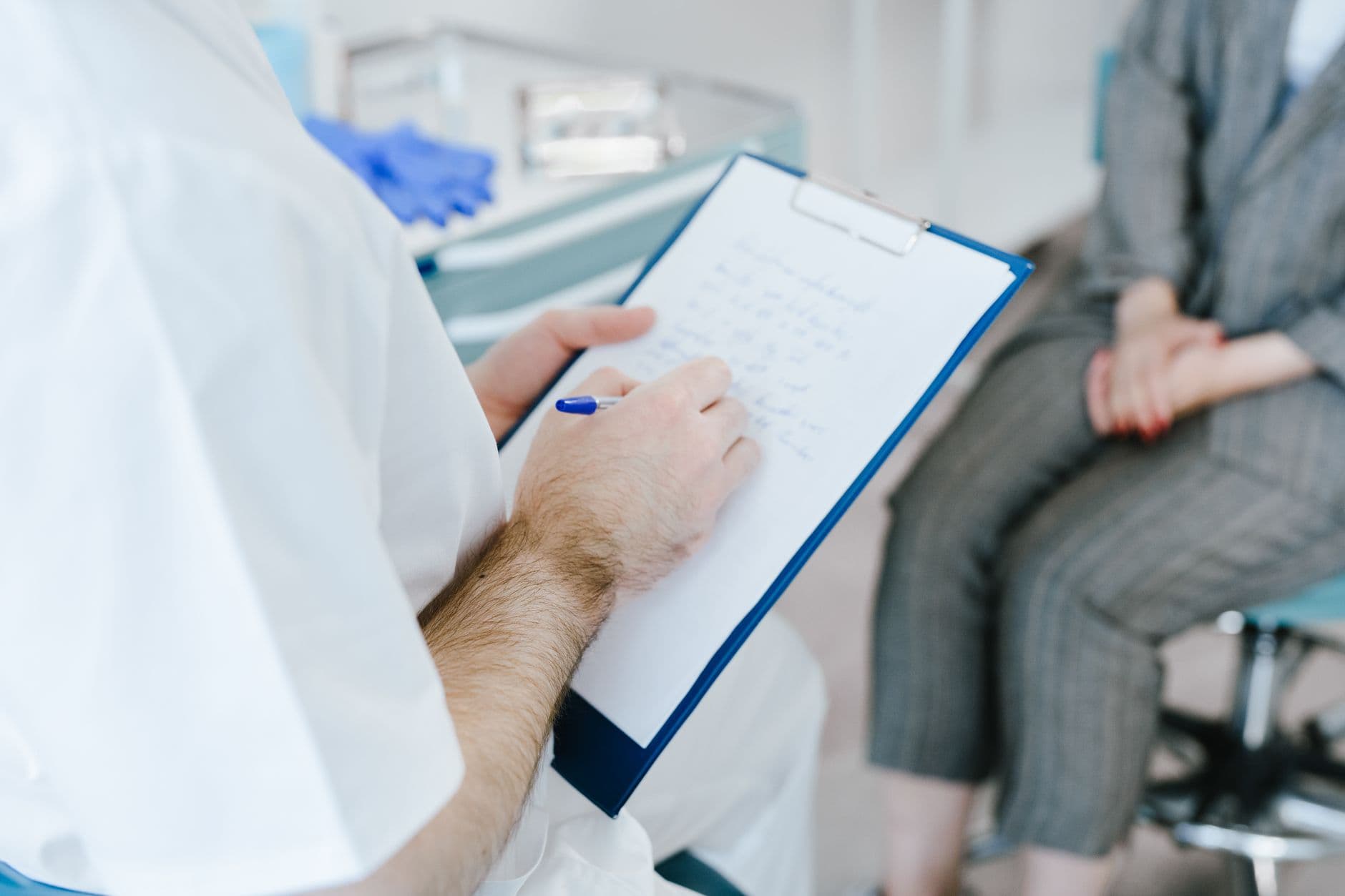 Website & Hosting for Doctors — Medical professional writing patient notes on clipboard during consultation.