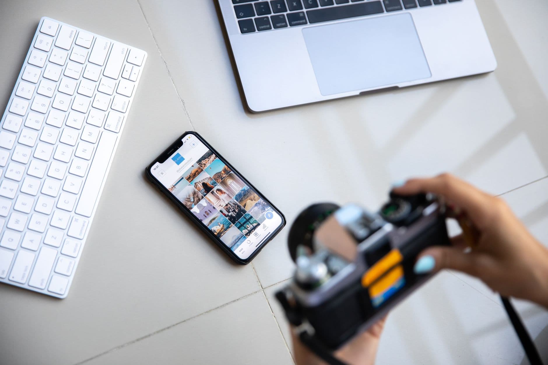 Social Media Management — Person using vintage camera with smartphone and laptop in creative setup.
