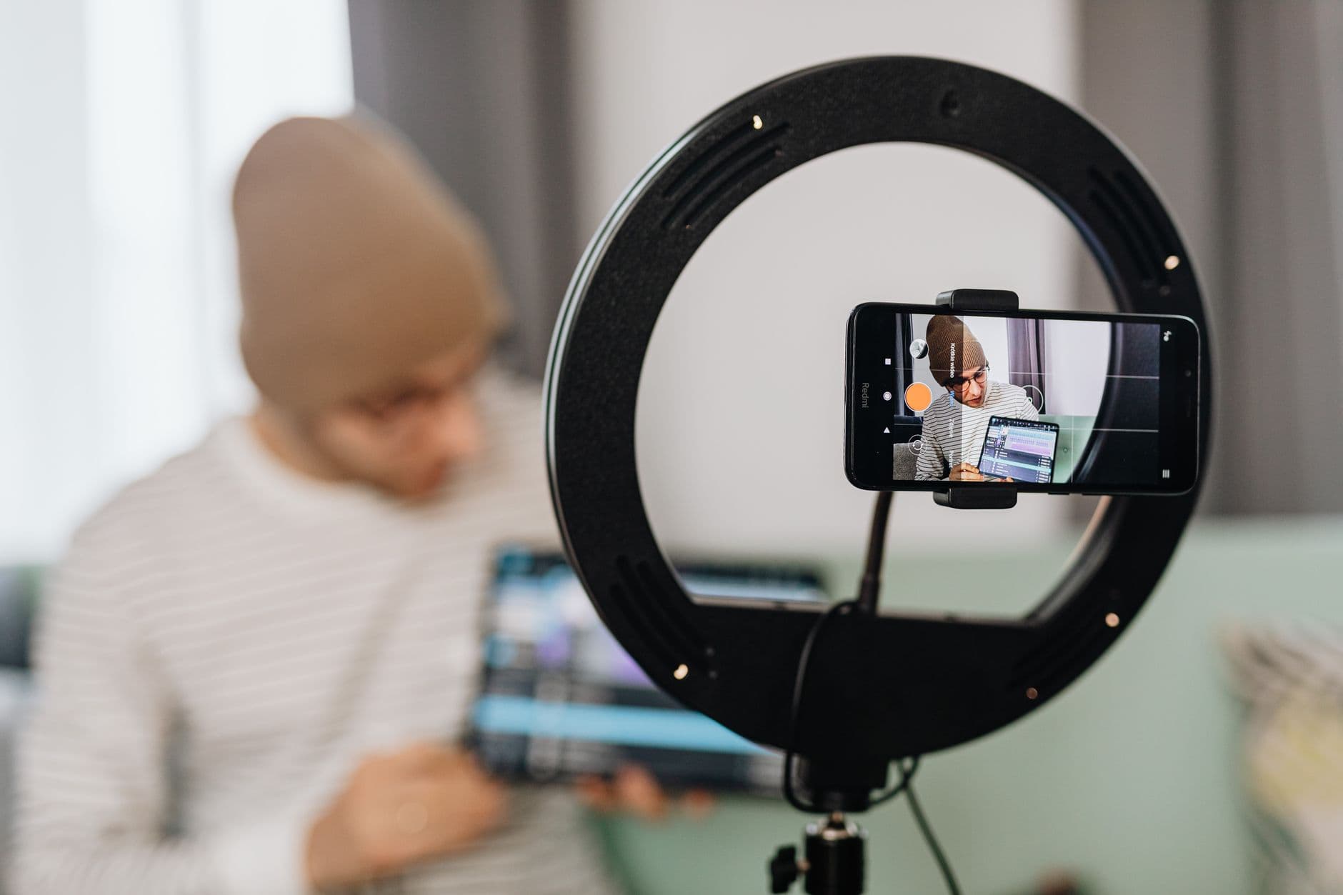 Social Media Management — Man vlogging with a smartphone and ring light, focused on content creation indoors.